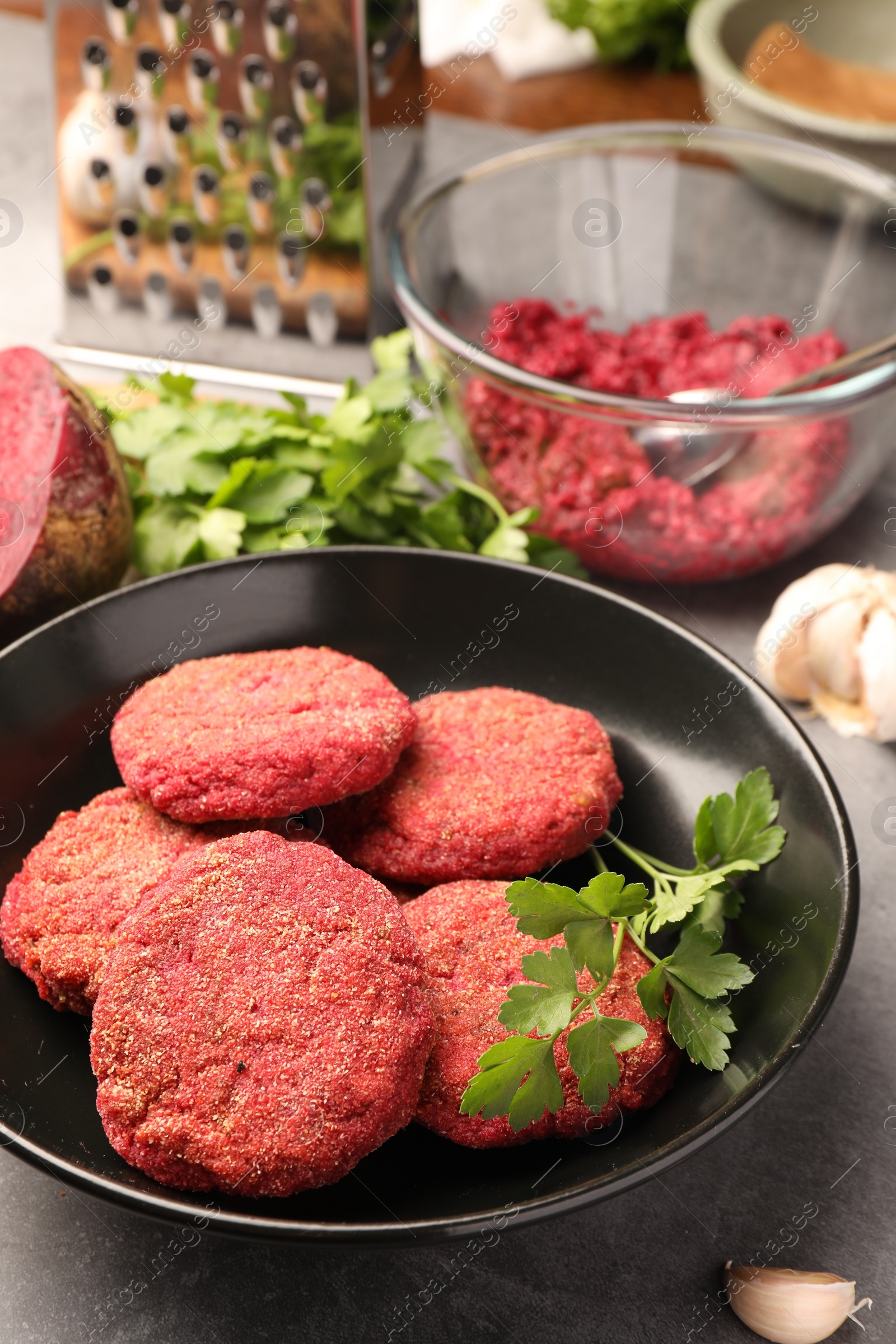 Photo of Delicious beetroot cutlets and parsley in black bowl on table. Vegan dish