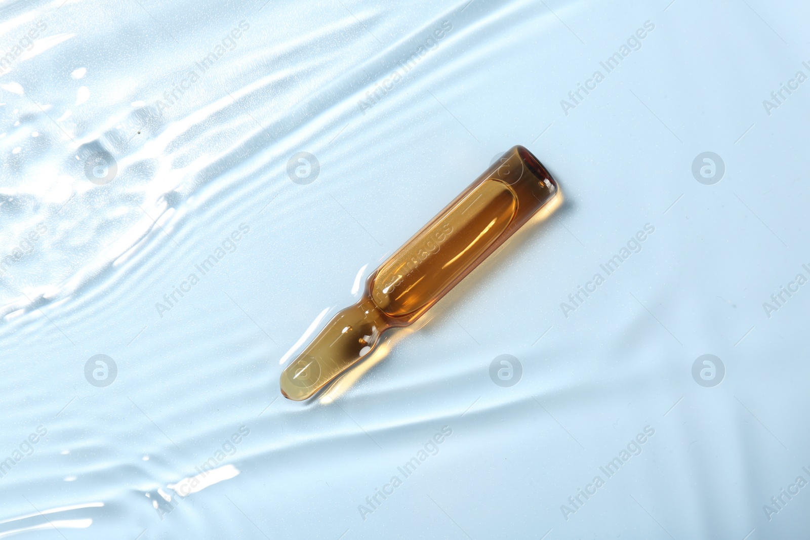 Photo of Skincare ampoule in water on light blue background, top view