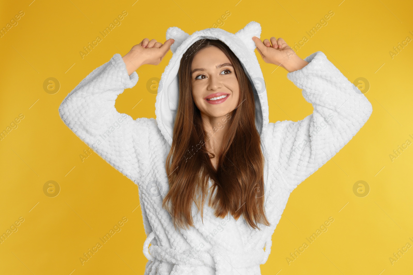 Photo of Beautiful young woman in bathrobe with funny hood on yellow background