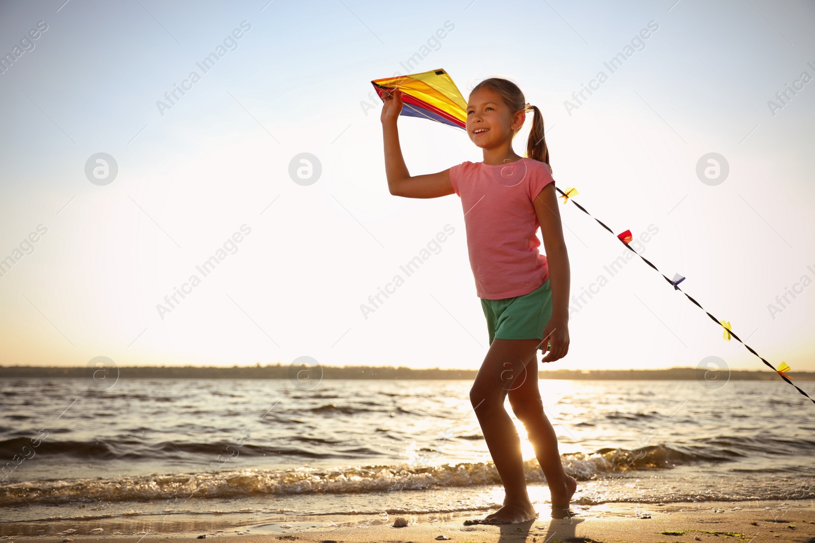 Photo of Cute little child playing with kite on beach near sea at sunset. Spending time in nature