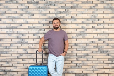 Photo of Man with suitcase near brick wall. Vacation travel