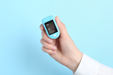 Photo of Woman holding modern fingertip pulse oximeter on light blue background, closeup
