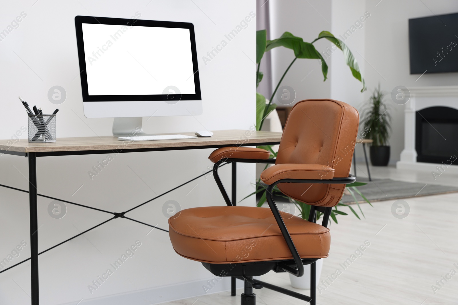 Photo of Comfortable office chair near desk and houseplants in modern workplace