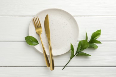 Photo of Stylish setting with cutlery, green leaves and plate on white wooden table, flat lay