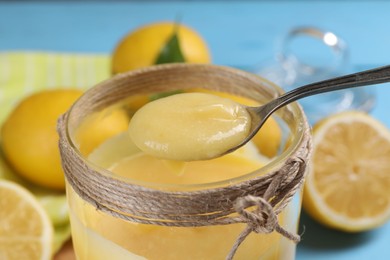 Taking delicious lemon curd from jar at light blue table, closeup