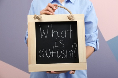 Photo of Woman holding blackboard with phrase "What is autism?" on color background