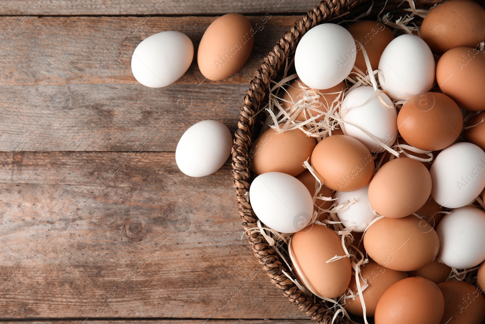 Photo of Basket with raw chicken eggs on wooden background, top view. Space for text