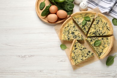 Photo of Cut delicious spinach pie with ingredients on white wooden table, flat lay. Space for text