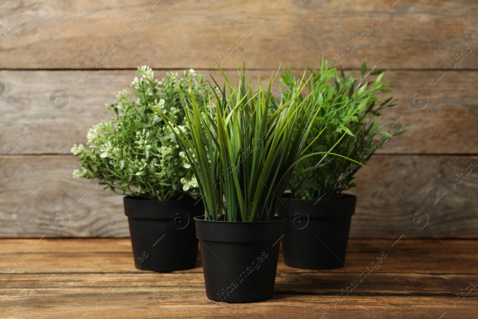 Photo of Artificial plants in black flower pots on wooden table