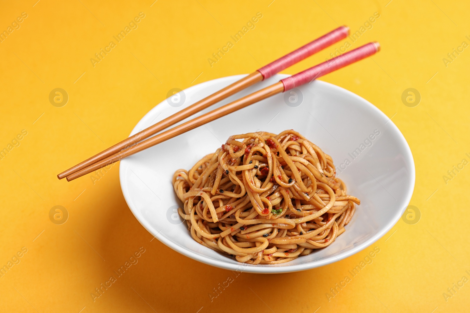 Photo of Bowl of cooked noodles and chopsticks on orange background