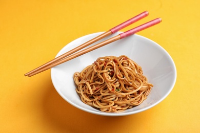 Bowl of cooked noodles and chopsticks on orange background
