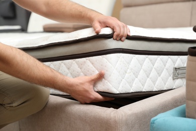 Photo of Young man choosing new orthopedic mattress in store, closeup