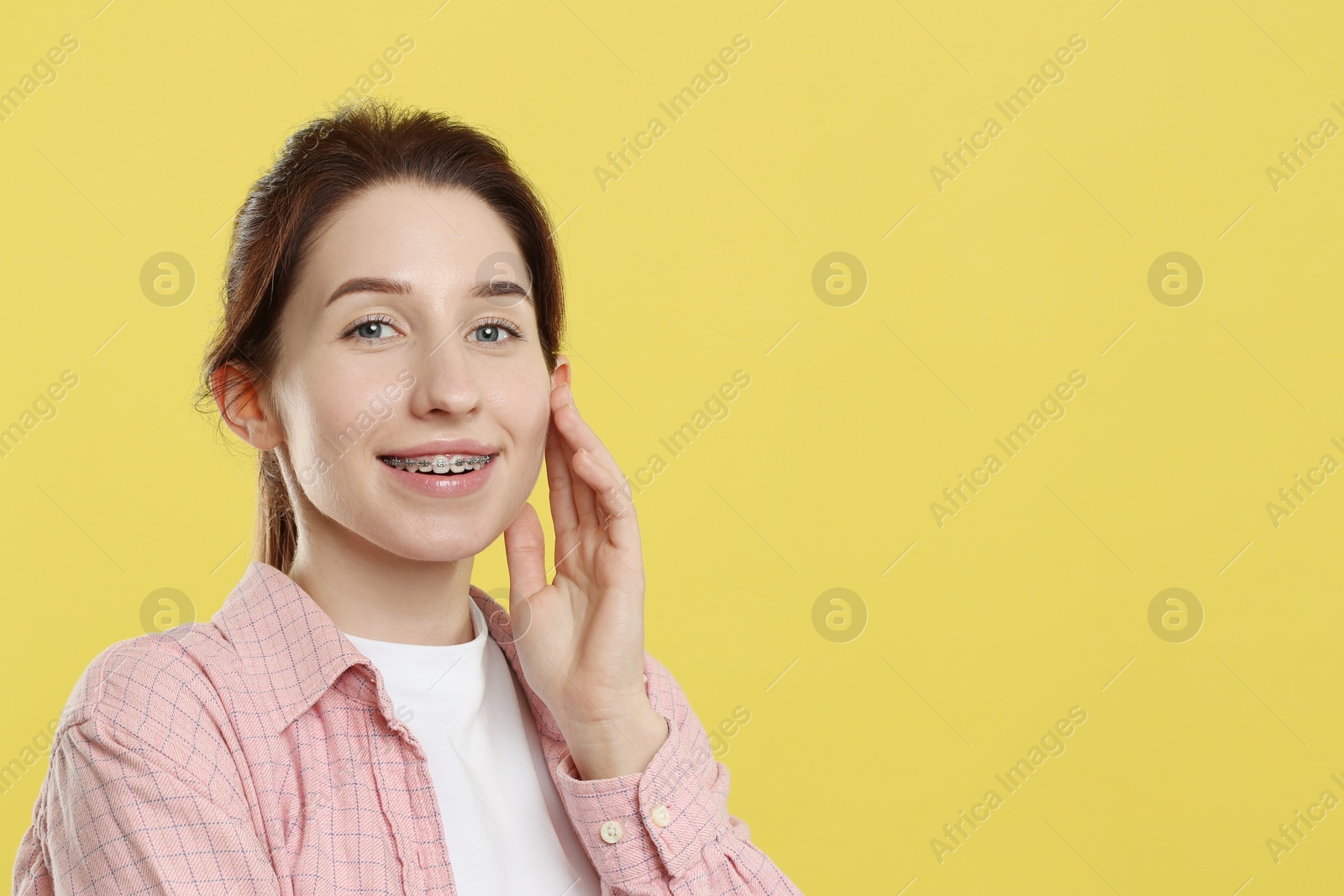 Photo of Portrait of smiling woman with dental braces on yellow background. Space for text