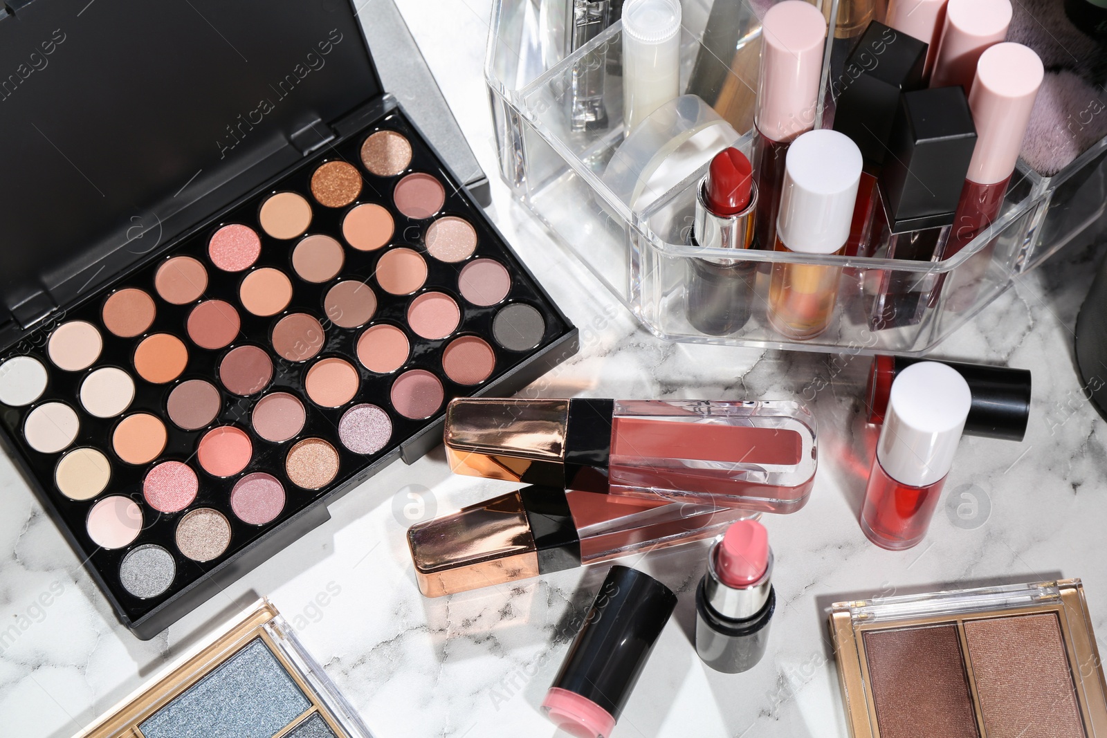 Photo of Bright lip glosses among different cosmetic products on white dressing table