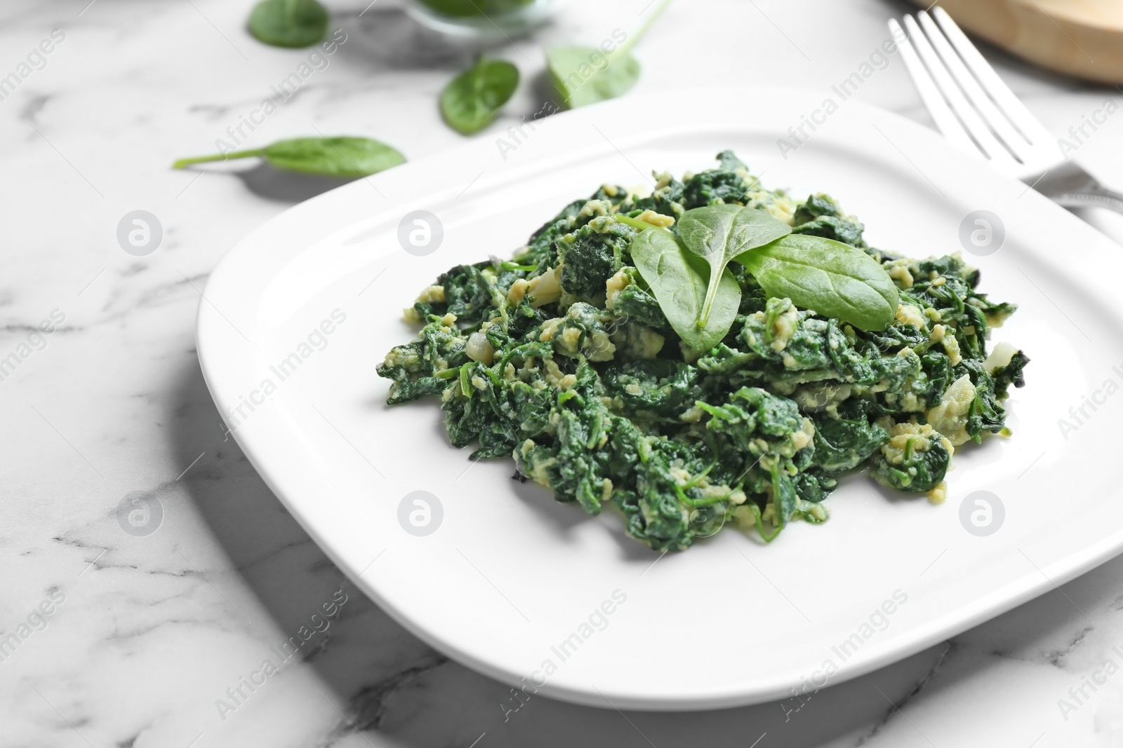 Photo of Tasty cooked spinach with scrambled eggs on white marble table, closeup. Healthy food