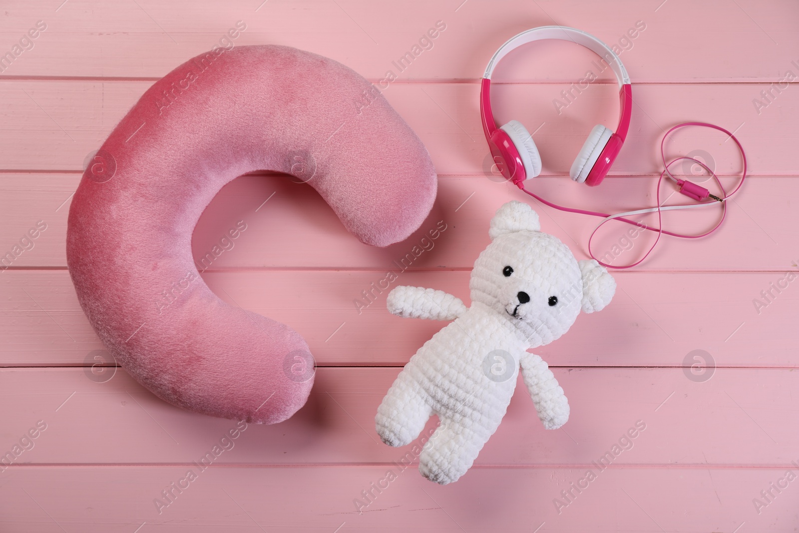 Photo of Travel pillow, toy bear and headphones on pink wooden background, flat lay