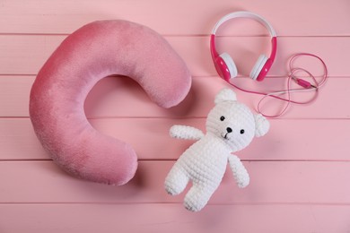 Photo of Travel pillow, toy bear and headphones on pink wooden background, flat lay