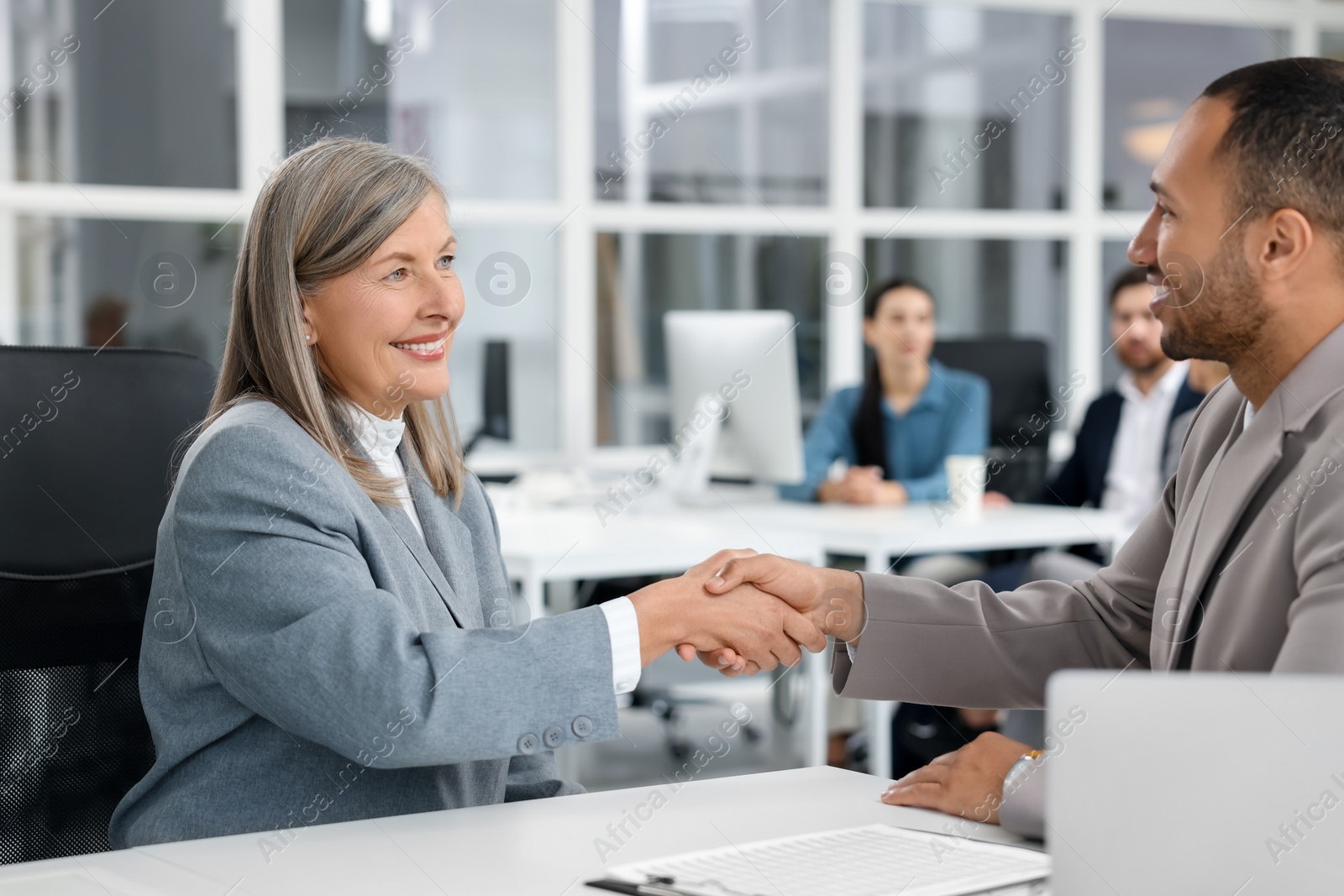 Photo of Lawyer shaking hands with client at table in office, selective focus