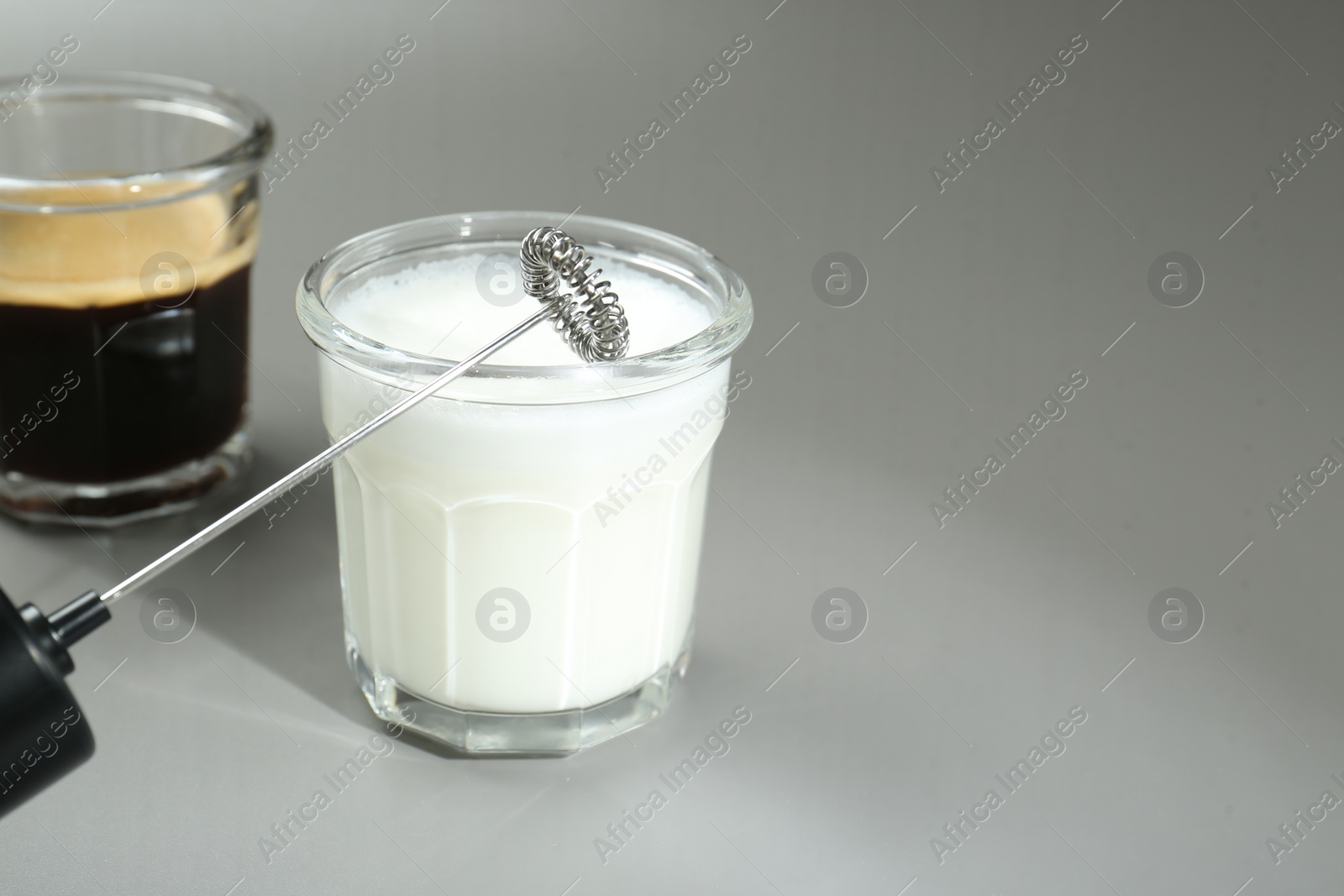 Photo of Mini mixer (milk frother), whipped milk and coffee in glasses on grey background, closeup. Space for text