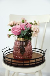 Beautiful bouquet of roses on chair near white wall