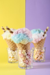 Sweet cotton candies in waffle cones and marshmallows on color background, closeup