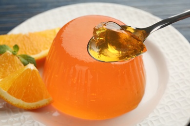 Photo of Spoon of tasty orange jelly over plate with dessert, closeup