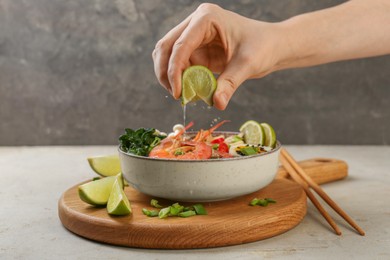 Woman squeezing lime juice into bowl of delicious ramen with shrimps at light textured table, closeup. Noodle soup