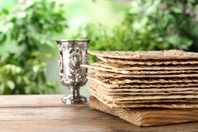 Photo of Traditional Matzos and silver goblet on wooden table, space for text. Pesach (Passover) celebration