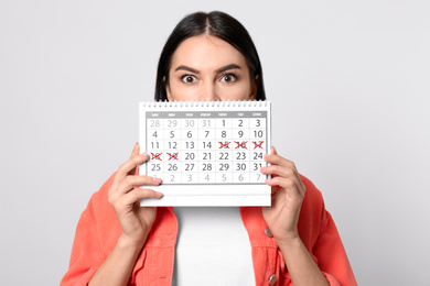 Photo of Young woman holding calendar with marked menstrual cycle days on light background