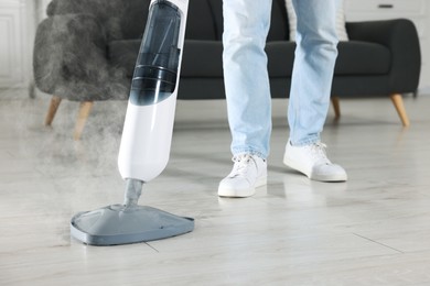 Photo of Man cleaning floor with steam mop at home, closeup