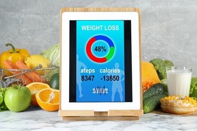 Tablet with weight loss calculator application and food products on white marble table