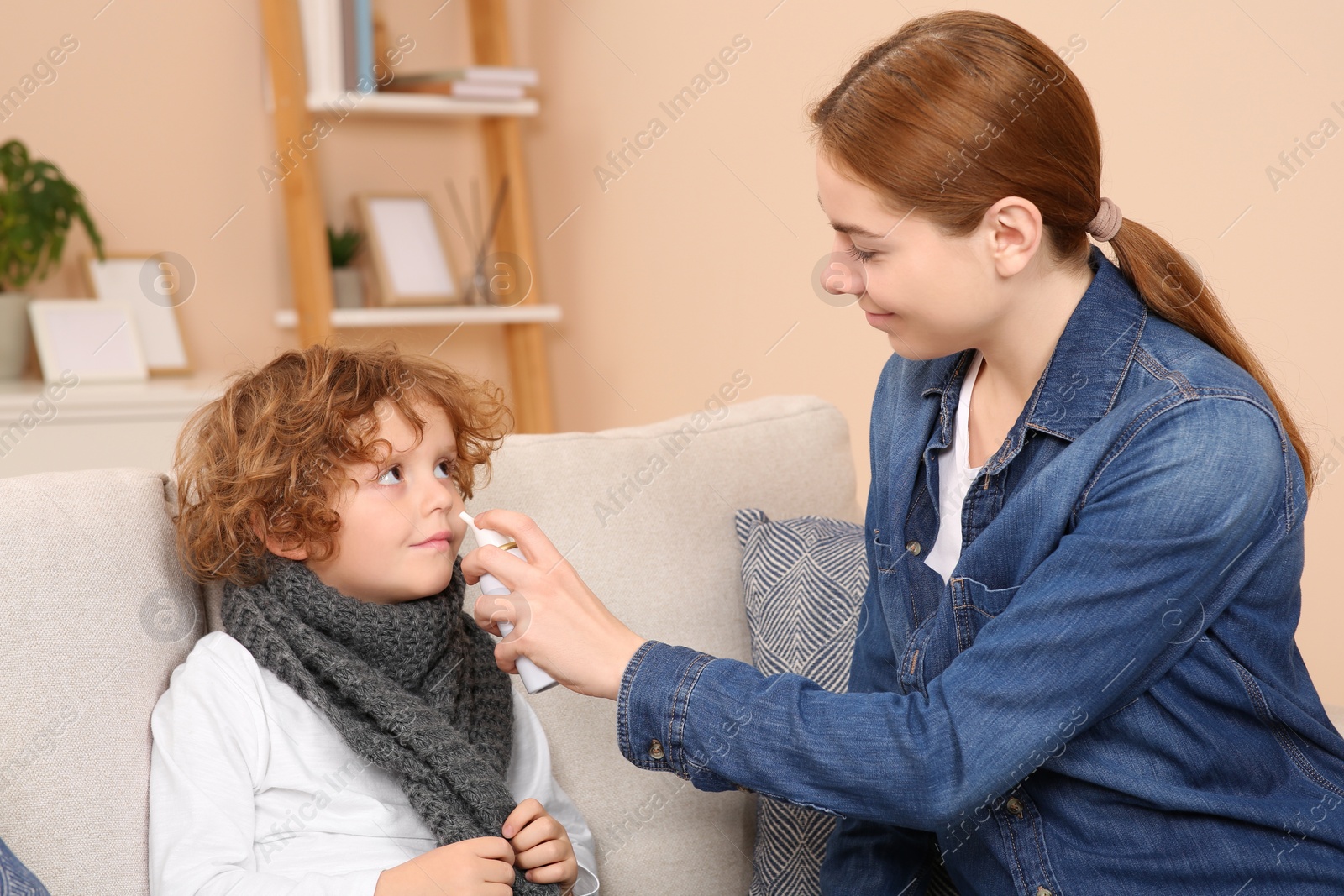 Photo of Mother using nasal spray to treat her little son on sofa indoors