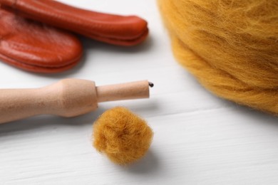 Photo of Orange woolen ball and needle felting tools on white wooden table, closeup
