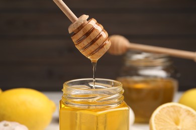Photo of Honey dripping from dipper into jar against blurred background, closeup