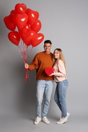 Photo of Lovely couple with heart shaped balloons and gift on grey background. Valentine's day celebration