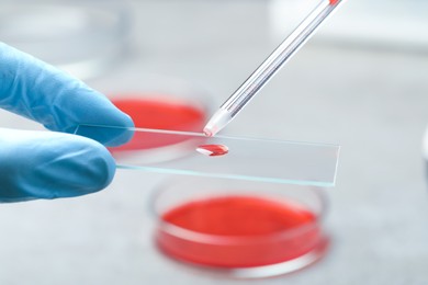 Scientist dripping sample of red liquid onto microscope slide in laboratory, closeup