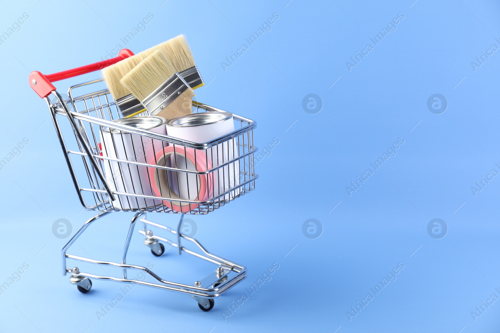 Photo of Small shopping cart with set of painting tools on light blue background. Space for text