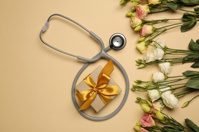 Photo of Stethoscope, gift box and flowers on dark beige background, flat lay. Happy Doctor's Day