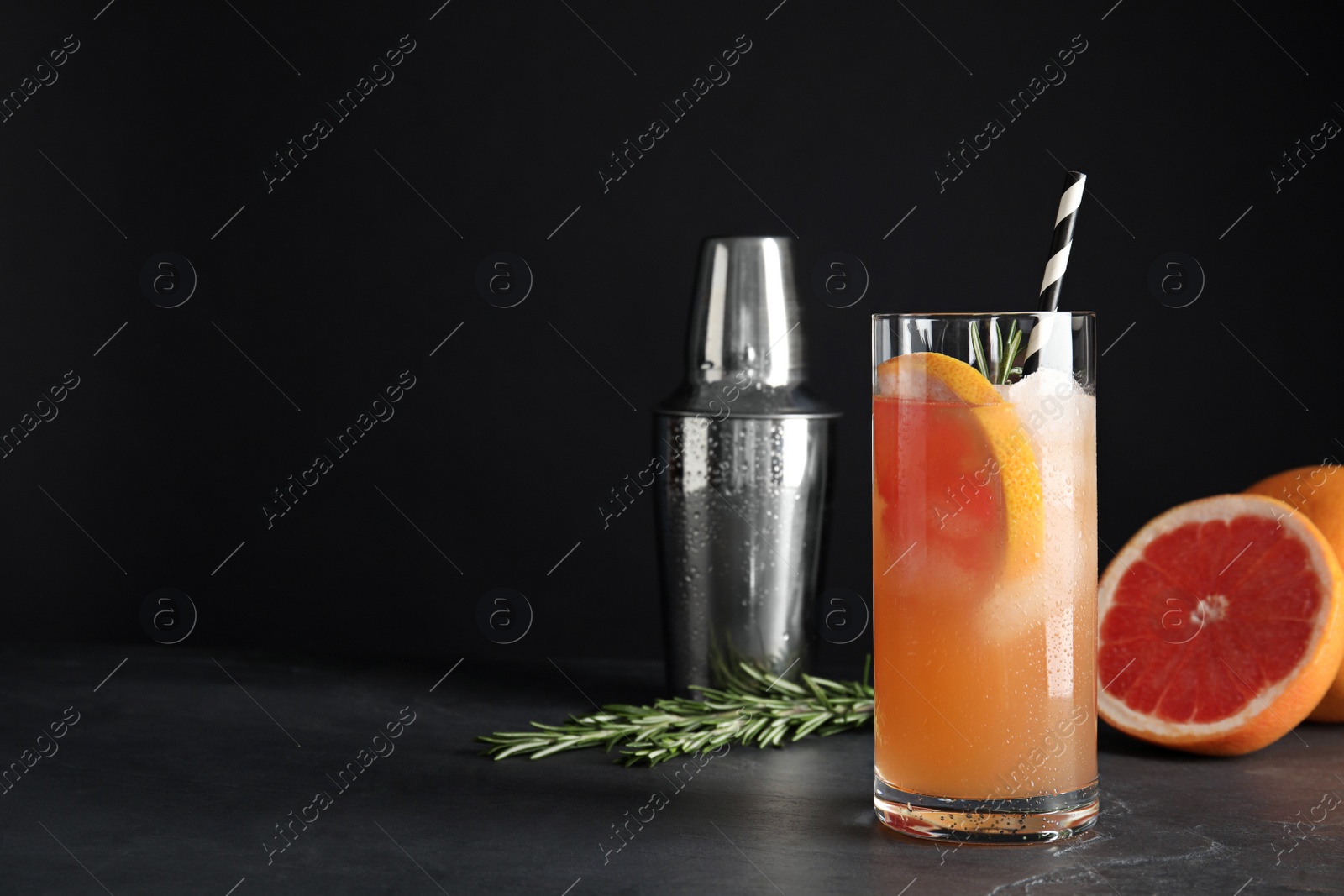 Photo of Glass of grapefruit cocktail served on table against black background. Space for text