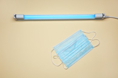 Photo of Ultraviolet lamp and medical masks on beige background, flat lay