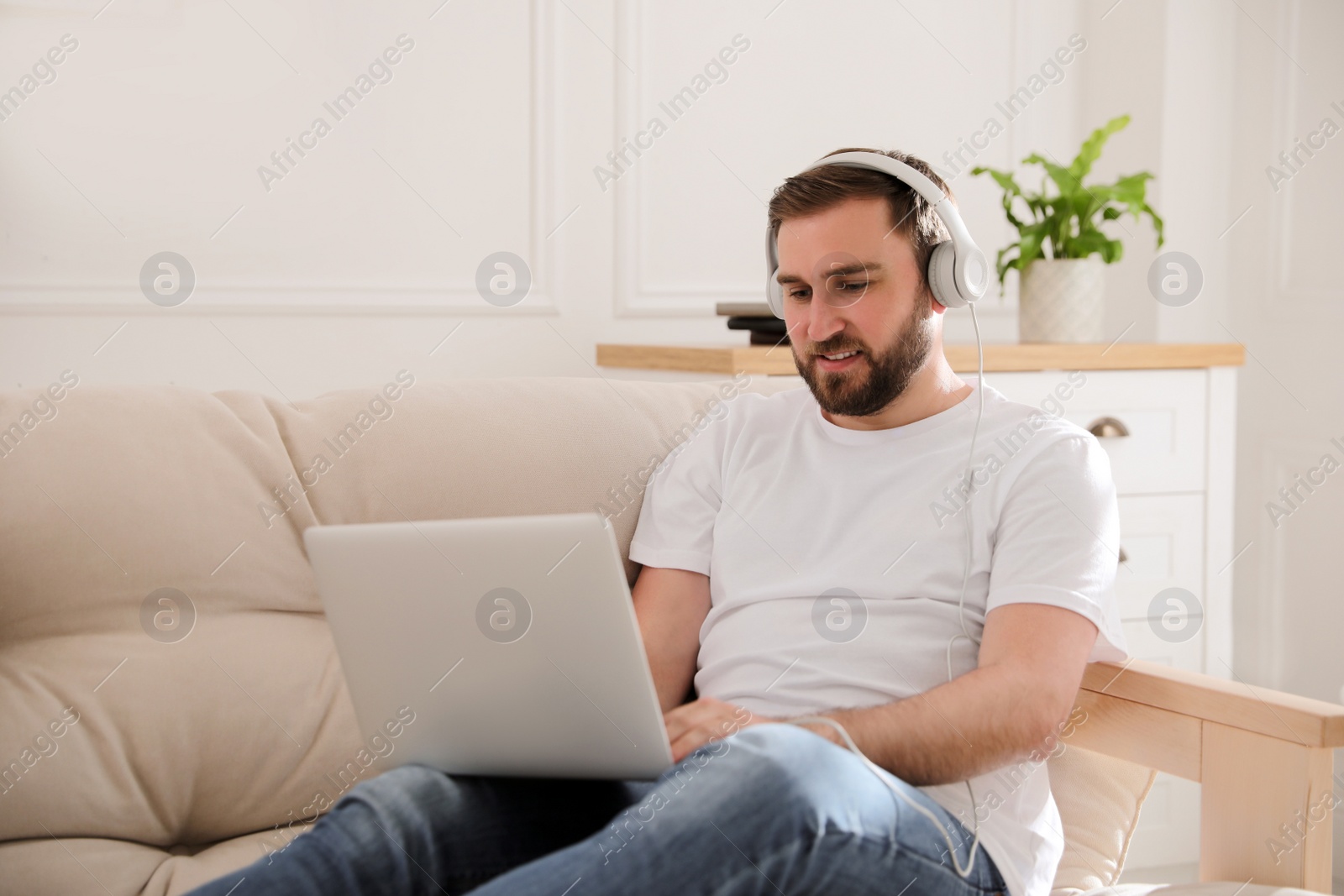 Photo of Man with laptop and headphones sitting on sofa at home