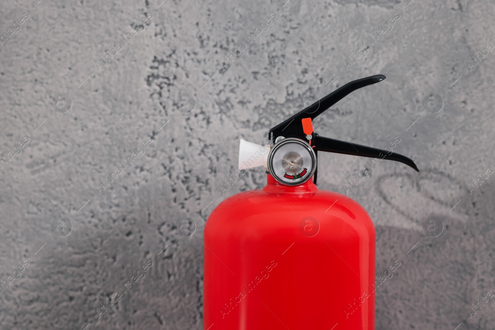 Photo of Red fire extinguisher near grey wall, closeup. Space for text