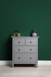 Photo of Modern chest of drawers with houseplants near green wall indoors