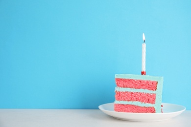 Slice of fresh delicious birthday cake with candle on table against color background. Space for text