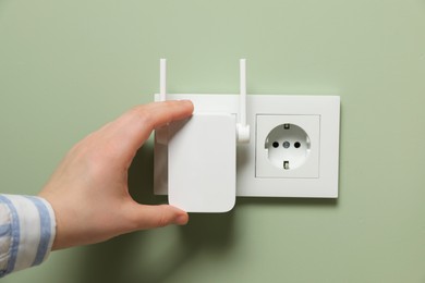 Woman turning on wireless Wi-Fi repeater near light green wall, closeup