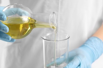 Developing cosmetic oil. Scientist pouring liquid from flask into beaker, closeup