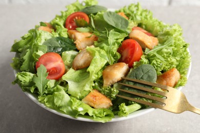 Photo of Eating delicious salad with chicken, cherry tomato and spinach at light grey table, closeup