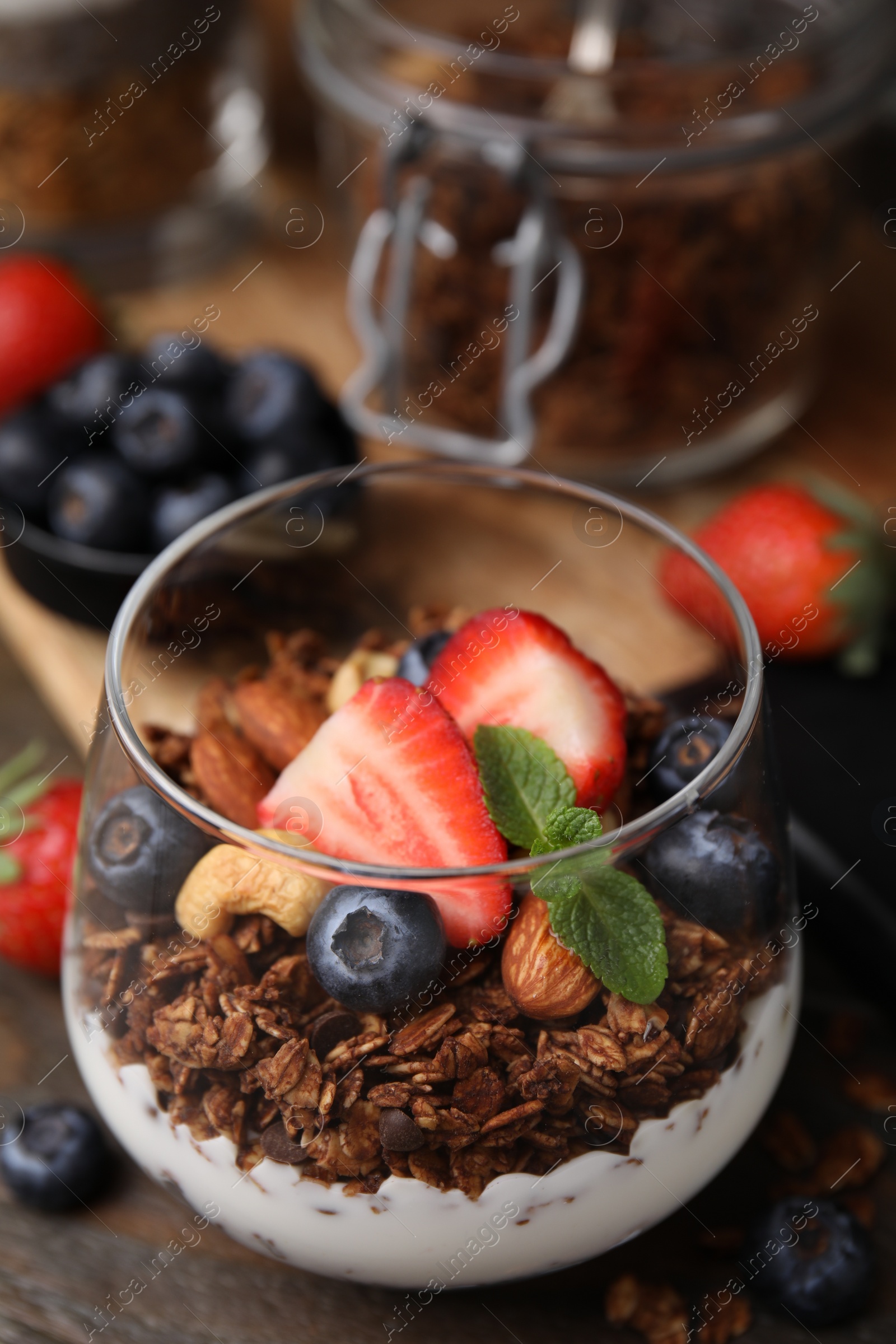 Photo of Tasty granola with berries, nuts and yogurt in glass on table, closeup