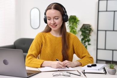 E-learning. Young woman taking notes during online lesson at white table indoors