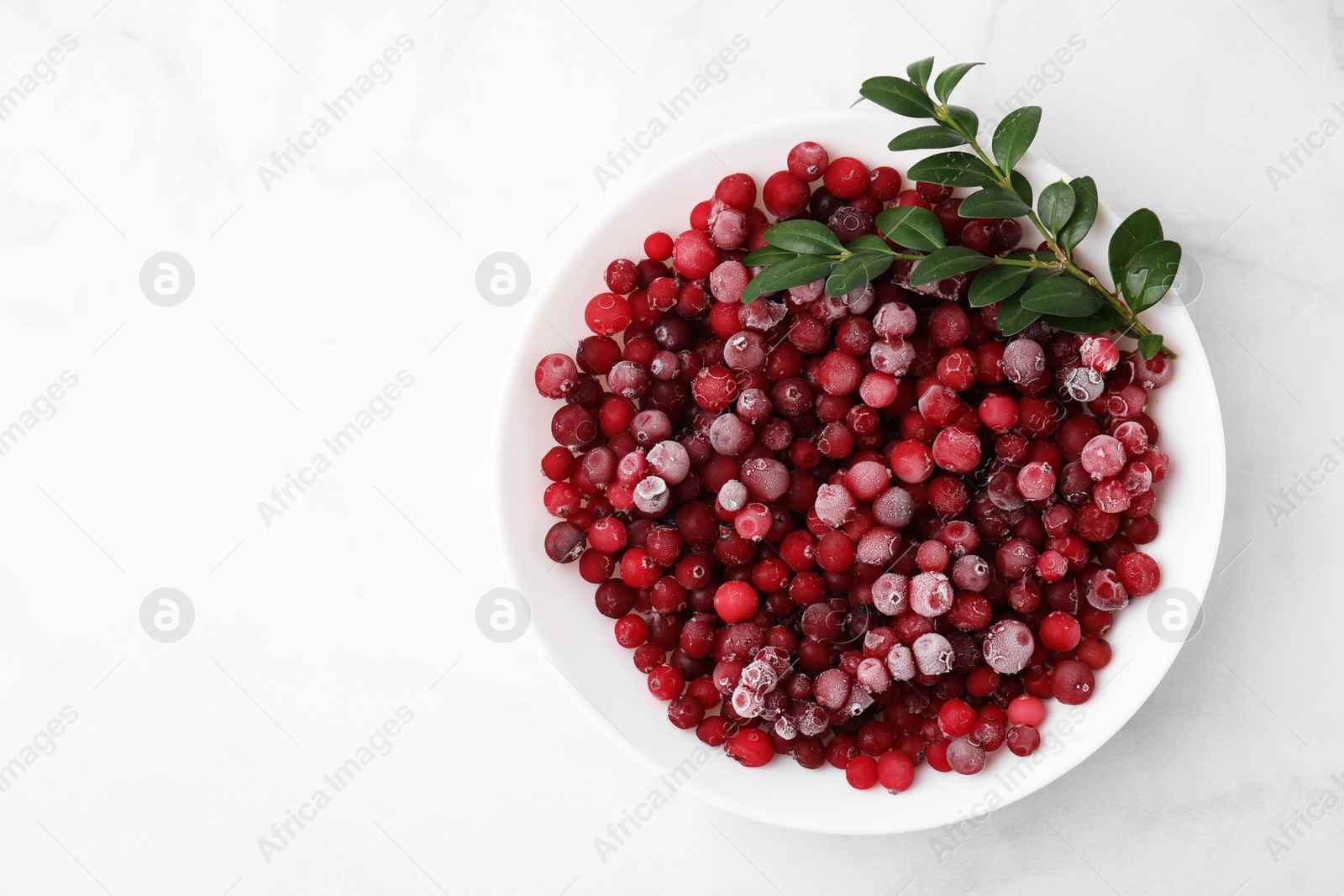 Photo of Frozen red cranberries and green leaves on white marble table, top view. Space for text